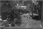 Mortuary ceremony: women weave long fiber skirts for ritual exchange, women in foreground tend cooking pots over fire