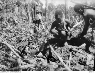 WEWAK AREA, NEW GUINEA, 1945-06-11. SGT R. AYRES, 2/8 INFANTRY BATTALION (1), SHOWING A JAPANESE PISTOL TO A NATIVE POLICE BOY. QUITE A FEW SOUVENIRS WERE FOUND IN CAPTURED ENEMY POSITIONS, DURING ..