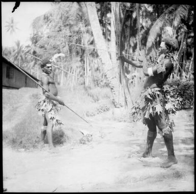 Two men wearing leafy skirts with one holding a spear and the other holding a bow and arrow, New Guinea, ca. 1936 / Sarah Chinnery