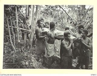 WAITAVALO AREA, WIDE BAY, NEW BRITAIN. 1945-03-16. AUSTRALIAN NEW GUINEA ADMINISTRATIVE UNIT NATIVES ASSIST WOUNDED OF HEADQUARTERS 6TH INFANTRY BRIGADE FROM THE RIDGES BEHIND WAITAVALO AND TOL ..