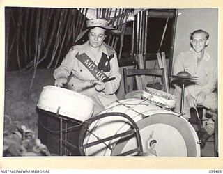 LAE AREA, NEW GUINEA, 1945-08-22. STAFF-SERGEANT D. LENTHOLL, AUSTRALIAN WOMEN'S ARMY SERVICE, SHOWING QUITE A LOT OF TALENT WHEN SHE GAVE THE LAE BASE ORCHESTRA DRUMMER A REST DURING THE MASKED ..