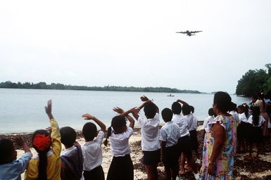 Children watch as a 374th Airlift Wing C-130 Hercules aircraft makes a low-level pass over Peleliu while delivering boxes of gifts to islanders of the Federated States of Micronesia. Flown by crews from the 345th and the 21st Airlift Squadrons, the C-130 is participating in Christmas Drop '92, the 40th anniversary of the humanitarian effort. Every Christmas since 1952, food, clothing, tools and toys donated by residents of Guam have been delivered by air to 40 Micronesian islands