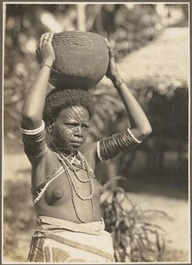 Girls from Village Wanigella [Wanigela], North Coast [Woman with a traditional facial tatooing on her face, carrying a pot on her head] Frank Hurley