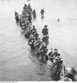 SANANANDA, NEW GUINEA, 1942-12-05. MEMBERS OF B COMPANY, 55/53RD BATTALION FORDING A RIVER. THE FIRST MAN IN LINE WITHOUT A HAT IS PRIVATE J. HUNTER AND THE NEXT THREE IN LINE ARE PRIVATES J. ..