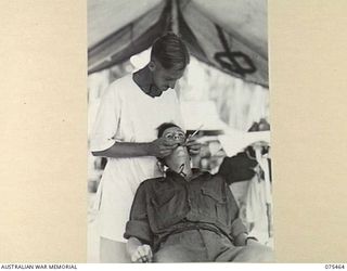 MILILAT, NEW GUINEA. 1944-08-23. NX111932 MAJOR R. MOORE, DENTAL OFFICER (1) FILLING A TOOTH FOR NX91797 LANCE CORPORAL K.C. PAINE (2) IN THE SURGERY OF THE 77TH DENTAL UNIT