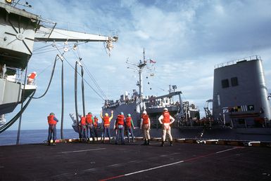 Crew members aboard the amphibious assault ship USS GUAM (LPH-9) prepare to transfer replenishment hoses to the tank landing ship USS LA MOURE COUNTY (LST-1194) as the two vessels are readied for an underway replenishment operation