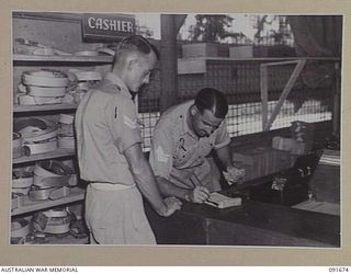 TOROKINA, BOUGAINVILLE. 1945-05-07. CORPORAL S.G. BOWDEN (1), HAS BILL CHECKED AND RECEIVES CHANGE FROM SERGEANT S.G. COUTTS, CASHIER (2), DURING A VISIT TO 4 SECTION OFFICERS' SHOP