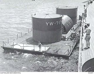 MILNE BAY, NEW GUINEA. C.1944. SELF PROPELLED WATER BARGE YW-717-? ALONGSIDE AN AUSTRALIAN CRUISER. (NAVAL HISTORICAL COLLECTION)