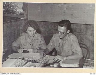 LAE, NEW GUINEA. 1945-05-15. CRAFTSWOMAN M.A. MACRITCHIE (1), RECEIVING TUITION IN HER NEW JOB AT THE CAMP COMMANDANT'S OFFICE, HEADQUARTERS LAE BASE SUB AREA, FROM SERGEANT A.A. FROST (2). A FEW ..