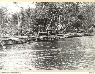 MOTUPENA POINT, BOUGAINVILLE ISLAND, 1945-01-26. A JEEP AND TRAILER OF THE 7TH INFANTRY BRIGADE CROSSING A TEMPORARY FLOATING BRIDGE ACROSS THE ADELE RIVER BUILT BY AUSTRALIAN ENGINEERS BY LASHING ..
