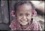 Young girl, Mogiovyeka's daughter, Imala, wearing red shell necklace, flowers, and dress