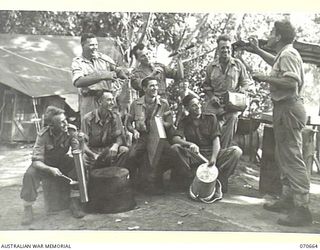 DALLMAN RIVER, NEW GUINEA, 1944-02-25. THE "COOKHOUSE SERENADERS", OF THE 231ST LIGHT AID DETACHMENT, USING COOKING UTENSILS AND A SHELL CASING FOR MUSICAL INSTRUMENTS. IDENTIFIED PERSONNEL ARE: ..