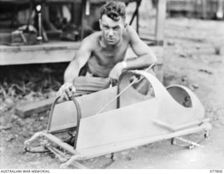 LAE BASE AREA, NEW GUINEA. 1944-12-27. VX146696 SAPPER L.F. HUNTER, 13TH WORKSHOPS AND PARK COMPANY, WITH A MODEL RACING CAR HE IS MAKING IN HIS SPARE TIME FROM SCRAP