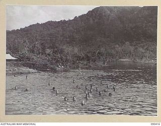 BUT, NEW GUINEA. 1945-04-02. TROOPS JUST OUT OF ACTION BATHE IN THE SEA NEAR THE AIRSTRIP. THESE PLEASANT SURROUNDINGS CONTRAST SHARPLY WITH THE RAZOR BACKED TORRICELLI MOUNTAINS IN THE BACKGROUND ..