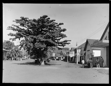 An Apia street scene with a group of boys outside the Morris Hedstrom Limited Cocoa Shed in foreground, Western Samoa