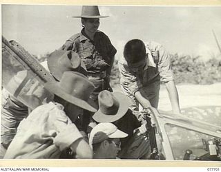 TOROKINA, BOUGAINVILLE ISLAND. 1944-12-23. WARRANT OFFICER J. REYNOLDS, NO.17 PHOTO SQUADRON, 13TH UNITED STATES AIR FORCE, EXPLAINING THE USE OF THE OXYGEN TUBE IN THE COCKPIT OF A P38 LOCKHEED ..