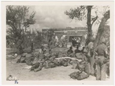 [Servicemen resting near destroyed building]