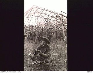 KAIAPIT, NEW GUINEA. 1943-09-23. SX17685 LANCE CORPORAL A. H. CLAYTON OF "D" COMPANY, 2/27TH AUSTRALIAN INFANTRY BATTALION PRIMES SOME HAND GRENADES IN PREPARATION FOR A PATROL. NOTE OLD BELL AND ..
