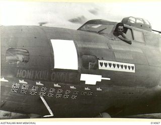 STAFF SERGEANT P. HOFFEOKER, OF DOVER, DELAWARE, USA, LOOKS OUT FROM HIS B-17 FLYING FORTRESS BOMBER. MARKINGS ON THE PLANE DENOTE ITS PAST PERFORMANCES. NAMED "HONI KUU OKOLE", WHICH IS HAWAIIAN ..
