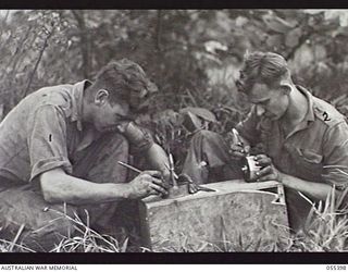 WAU, NEW GUINEA. 1943-08-9-12. CORPORAL (CPL) J. ROBSON (LEFT) AND CPL G. E. PARR MAKING ASH TRAYS FROM OLD ARTILLERY SHELLS AND .303 CARTRIDGES