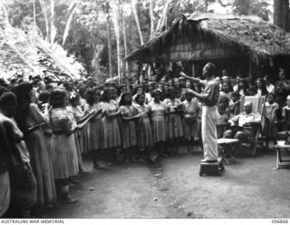 Ramale Valley, New Britain. A choir comprised of the internees at Ramale Valley Internment Camp singing 'Minstrel Boy' for Major General K W Eather, General Officer Commanding 11 Division. Contact ..