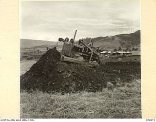 WAU, NEW GUINEA, 1944-02-23. WX26402 PRIVATE N.M. GRAY (1), OF THE 2/4TH FIELD SQUADRON USING A BULLDOZER TO CUT A ROAD THROUGH THE REST CAMP AREA. THE AIRSTRIP LIES IN THE BACKGROUND