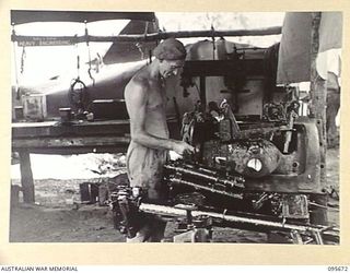 BOUGAINVILLE. 1945-08-30. CORPORAL P. GUILFOYLE, 2/4 ARMOURED REGIMENT WORKSHOP GREASING PARTS OF A 2-POUNDER TANK GUN THAT HAD BEEN REMOVED FROM A MATILDA TANK, KNOCKED OUT BY THE JAPANESE EAST OF ..