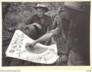 WEWAK AREA, NEW GUINEA. 1945-10-13. SERGEANT T. NISBET (1), DRIVER D.R.S. COOMBS (2) AND CORPORAL G.F. GIBSON (3) MEMBERS OF 3 MOBILE TYRE WORKSHOP SECTION, EXAMINING A JAPANESE FLAG FOUND IN THE ..