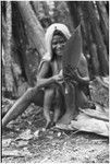 Pig festival, pig sacrifice, Tsembaga: woman, holding infant, flattens leaves for thatching sacrifice house