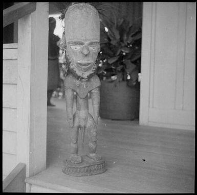 Full figure carving with an elongated head, on a verandah, Awar [?], Sepik River, New Guinea, 1935, 1 / Sarah Chinnery