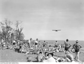 LAE AREA, NEW GUINEA. 1944-11-26. A PIPER CUB AIRCRAFT OF THE RAAF SWOOPS LOW OVER THE AUSTRALIAN AND ALLIED SERVICE PERSONNEL ENJOYING A SWIM IN THE WARM WATERS OF THE HUON GULF WHILE ON A SHARK ..