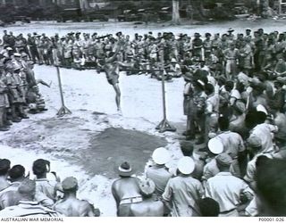 THE SOLOMON ISLANDS, 1945-01-12. SPECTATORS ENGROSSED WATCHING THE HIGH JUMP AT A COMBINED ANZAC SPORTS MEETING AT BOUGAINVILLE ISLAND. (RNZAF OFFICIAL PHOTOGRAPH.)