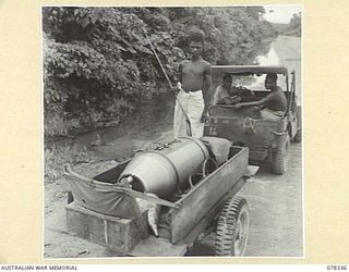TOROKINA, BOUGAINVILLE ISLAND. 1945-01-17. NX120943 CORPORAL W.G. JONES, 2/1ST MALARIAL CONTROL UNIT AND HIS TWO NATIVE HELPERS OPERATING A PRESSURE TANK FROM A JEEP TRAILER WHILE SPRAYING AREAS OF ..