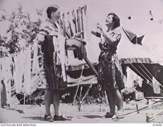 1943-04-01. AUSTRALIAN NURSES IN NEW GUINEA. WASHING LINES STRUNG BETWEEN TENTS. SISTER M. ALCORN OF MANLY, QUEENSLAND, HOLDS THE CLOTHES WHILST SISTER SHEILA DITTY OF TERANG, VICTORIA, PEGS THEM ..