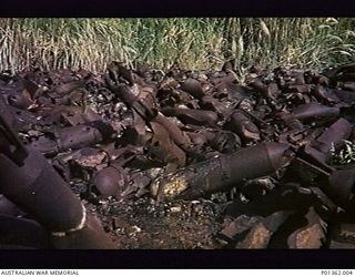 DOBODURA, PAPUA. 1951. AMERICAN MUSTARD GAS BOMBS LYING AT THE END OF THE AIRSTRIP AT EMBI. THE BOMBS HAVE BEEN IGNITED, POSSIBLY TO ASSIST SCAVENGERS TO SALVAGE SCRAP METAL. (DONOR M. KEARY)