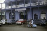 French Polynesia, woman driving scooter past Import Export Commission in Papeete