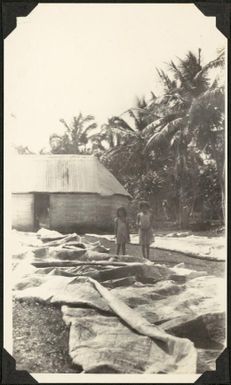 Two children stand near large textile pieces, Samoa, 1929 / C.M. Yonge