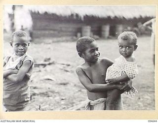 SIPILANGAN, NEW BRITAIN, 1945-08-01. A NATIVE BOY NURSING A PICCANINNY AT THE AUSTRALIAN NEW GUINEA ADMINISTRATIVE UNIT DISTRICT SERVICES TOL REFUGEE CAMP. THE CAMP, SITUATED AT WIDE BAY, HOUSES ..