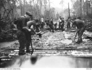 SOUTH BOUGAINVILLE, 1945-07-20. TROOPS OF 58/59 INFANTRY BATTALION WORKING IN THE RAIN REPAIRING THE BUIN ROAD. AS THIS IS OUR MAIN SUPPLY ROUTE IT IS ESSENTIAL TO GET SUPPLIES THROUGH. SECTIONS ..