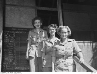 LAE, NEW GUINEA, 1945-05-15. LANCE-CORPORAL P.E. NICHOLLS (1), SAPPER M.E. ANDERSON (2), AND SERGEANT W.M. BENNETT (3), STANDING ON THE STEPS OF THE TWO-STOREY, GRASS-ROOFED HUT WHERE THEY WORK AT ..