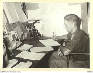 BOUGAINVILLE ISLAND. 1945-01-20. VX83223 LIEUTENANT T.J. DAVIES, BATTERY OFFICER, 2ND FIELD REGIMENT, IN HIS OFFICE CHECKING THE REPORTS OF THE NIGHTS OPERATIONS