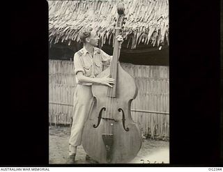 AITAPE, NORTH EAST NEW GUINEA. 1945-04-03. STANDING WITH THE BASE MUSICAL INSTRUMENT IS FLIGHT LIEUTENANT S. FLETCHER, OF EAST MELBOURNE, VIC, THE RAAF AREA WELFARE OFFICER IN NORTHERN NEW GUINEA, ..