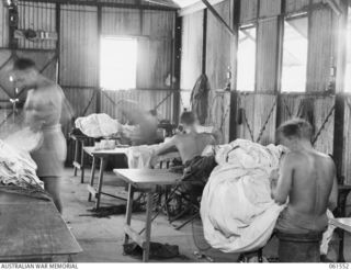 3 MILE, PORT MORESBY, NEW GUINEA. 1943-12-14. NX82290 CORPORAL K. J. WATSON (1) OF THE 1ST AUSTRALIAN PARACHUTE REFOLDING PLATOON, AUSTRALIAN ARMY ORDNANCE CORPS, INSPECTS A DAMAGED PARACHUTE ..