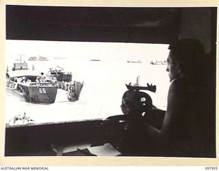 WEWAK BEACH, NEW GUINEA. 1945-10-18. PRIVATE R. HORNE, 8 PORT OPERATING COMPANY, INSIDE THE CONTROL TOWER RECEIVING MESSAGES FROM THE PORT OPERATING OFFICER, WHO IS ON THE CARGO SHIP IN THE PORT, ..