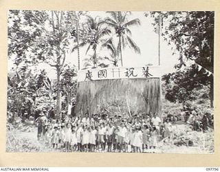 RATONGOR, NEW BRITAIN, 1945-10-10. CHINESE CHILDREN OF ALL SHAPES AND SIZES LINE UP OUTSIDE THE GAILY DECORATED ENTRANCE TO THE CAMP TO WAIT THE ARRIVAL OF THE NATIVE BAND. MEMBERS OF 11 DIVISION ..