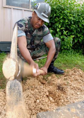 US Navy PETTY Officer 2nd Class Jason Maxwell, a Seabee assigned to Naval Facilities Engineering Command Marianas, uses a pick to clear dirt from a concrete antenna footer during a construction project at Naval Base Guam.(U.S. Navy photo by Mass Communication SPECIALIST 2nd Class John F. Looney) (Released)