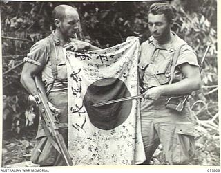 1943-09-25. NEW GUINEA. OUTSIDE LAE. U.S. PARATROOPERS WHO JOINED UP WITH THE AUSTRALIANS SHOW A JAPANESE FLAG CAPTURED AT EDWARDS CREEK. LEFT TO RIGHT - SGT. MIKE HOSTINSKI OF ADENA, OHIO, C/1 ..