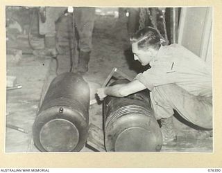 LABU, NEW GUINEA. 1944-10-03. CORPORAL J.C. JURD, 1ST WATERCRAFT WORKSHOPS, INSPECTING ONE OF THE BADLY DAMAGED PISTONS FROM THE ENGINE OF THE "FRANCES PEAT". THE "FRANCES PEAT" IS A COMPARATIVELY ..