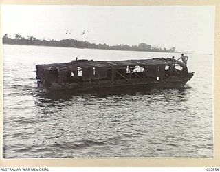 PURUATA ISLAND, SOUTH BOUGAINVILLE. 1945-05-29. A SALVAGED AUSTRALIAN LANDING CRAFT 5, NEARLY SWAMPED, AWAITING TOW BY 42 LANDING CRAFT COMPANY TO PURUATA ISLAND