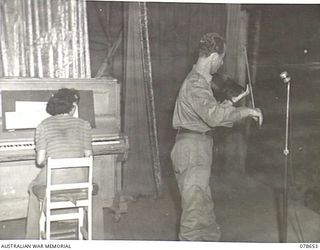 LAE AREA, NEW GUINEA. 1945-01-28. THE FAMOUS AUSTRALIAN COMEDIAN, DICK BENTLEY, LEADER OF THE DICK BENTLEY CONCERT PARTY ENTERTAINING THE TROOPS WITH HIS JOKES AND VIOLIN DURING A SHOW STAGED BY ..